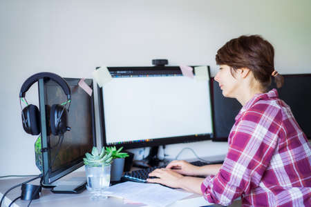 Side view woman working on pc with few monitors at home working space. Remote work concept....