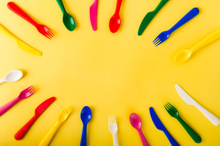 Oval frame made of reusable cutlery on the yellow background. Plastic spoons, forks, knives top...
