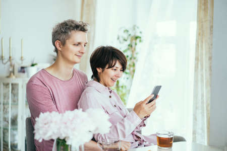 Portrait of happy couple man and woman using smartphone while sitting at the table together during...