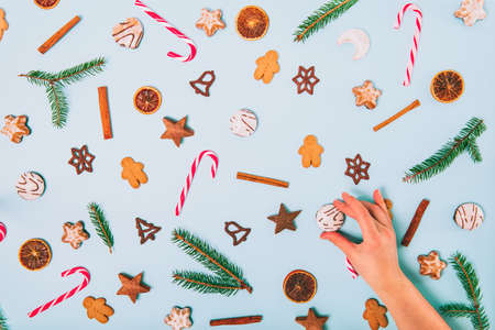 Top view background of Christmas sweets on the blue surface and female hand putting or taking one of...