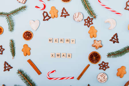 Top view Christmas wreath made of different varieties of Christmas cookies, candies, candy canes, dried oranges, gingerbread sweets on the blue background. Merry Christmas lettering.の写真素材