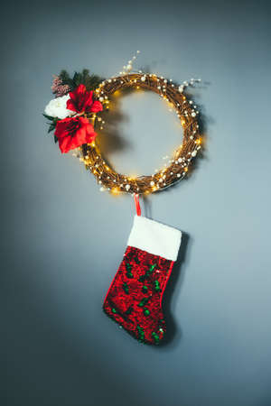 Modern flower wreath made of woven branches, pearls and lights with hanging red sequins Christmas stockings on the gray wall. Minimalist festive decor. Scandinavian style. Vertical card. Copy spaceの写真素材