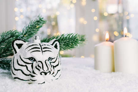 Tiger symbol of the Chinese new year 2022. Figurine of a tiger head on the artificial snow with burning candles and fir tree branch on bokeh lights background. Festive card. Copy spaceの写真素材