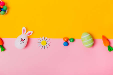 Top view festive Easter pink and yellow background with colored eggs, decorative carrots, bunny rabbits, flowers, chocolate eggs. Creative bright Easter. Flat lay. Copy space.の写真素材
