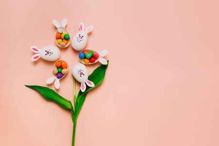 Top view Easter pink beige background with flower shape made of funny eggs containers with bunny ears filled with candy chocolate eggs. Bunny rabbit symbol. Easter egg hunt. Creative Easter.の写真素材