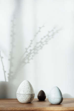 Home interior with easter decor. Pussy willow branches in a vase, easter eggs statuettes on the wooden console with light and shadow background. Minimalism, scandinavian style. selective focus.の写真素材