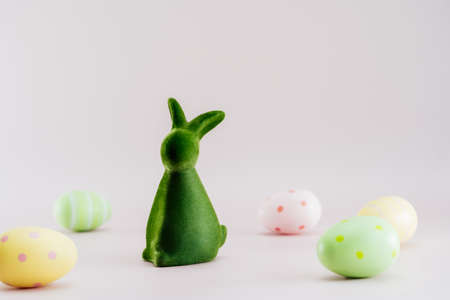 Green bunny rabbit figurine and colored easter eggs in different patterns on neutral pink background. Festive Ester spring card mockup. Selective focus. Copy space.の写真素材