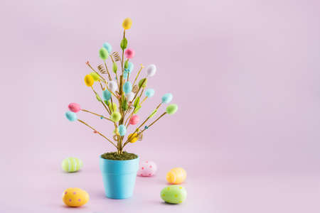 Easter tree decor in blue pot with colorful eggs around on the light pink background. Minimalist...