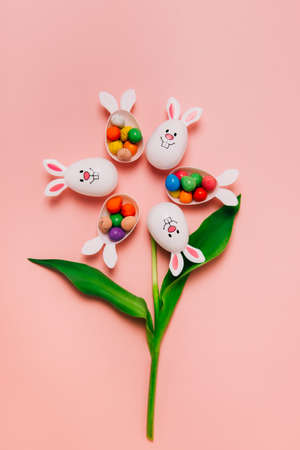 Top view Easter pink background with flower shape made of funny eggs containers with bunny ears...