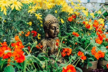 Bronze Gautama Buddha decorative statue in a garden with red and yellow flowers. Exterior, Outdoor...