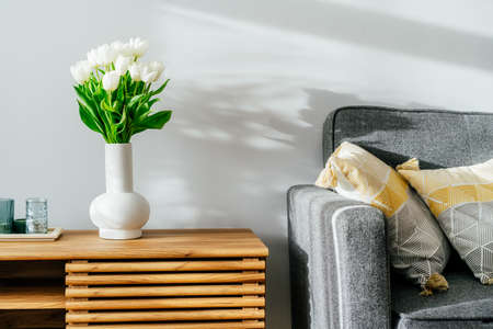 Scandinavian home interior with spring bouquet of white tulip flowers in glass vase, tray with...