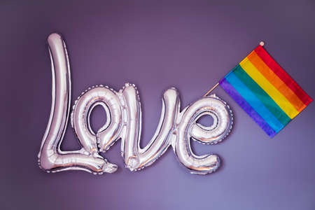 Love word of a silver foil balloon with LGBTQ rainbow flag on purple background. Happy Pride month. Declaration of different kinds of love. LGBT rights. Selective focusの写真素材