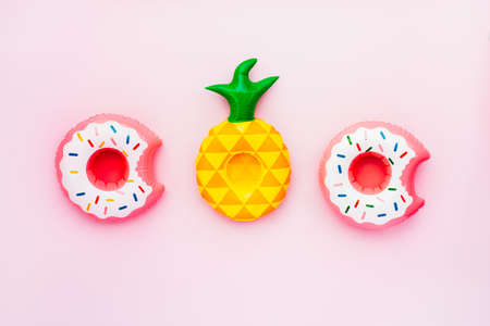 Top view inflatable toy rings on pink Background. Drinks Holders for Swimming Pool Party in Shape of Donuts and pineapple. Flat lay, selective focus, copy space.の写真素材