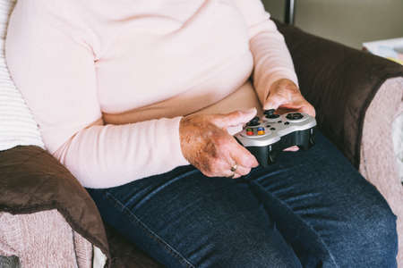 Close up senior, mature woman hands using wireless controller, joystick gamepad playing video games at home. Fun on Retirement. Gaming hobby. Technology, entertainment industry.の写真素材