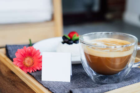 Cup of coffee, Pavlova dessert cake, gerbera flower and blank postcard with copy space on the tray...