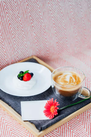 Cup of coffee, Pavlova dessert cake, gerbera flower and blank postcard with copy space on the tray with gray napkin. Breakfast for loved one. Romantic surprise. Take a break, relax. Selective focus.の写真素材