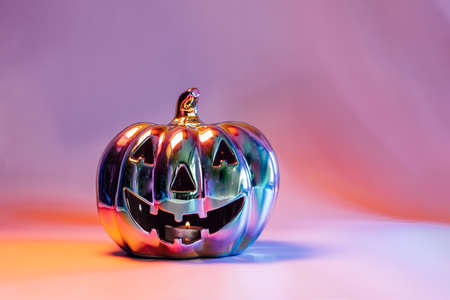 Spooky halloween pumpkin, Jack O Lantern, with an evil face and eyes made of holographic glass in neon lighting on pink background with copy space. Happy Halloween decoration conceptの写真素材