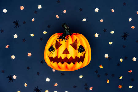 Top view bright Halloween background with carved orange pumpkin. Halloween Jack-o-lantern with spiders on it and multicolored autumn tinsel on the dark blue background. Flat lay. Selective focus.の写真素材