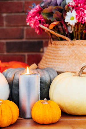 Festive composition for autumn holidays. Burning candle, various pumpkins and flowers bouquet in the wicker basket on brik wall background. Thanksgiving or Halloween. Fall Harvesting. Selective focusの写真素材