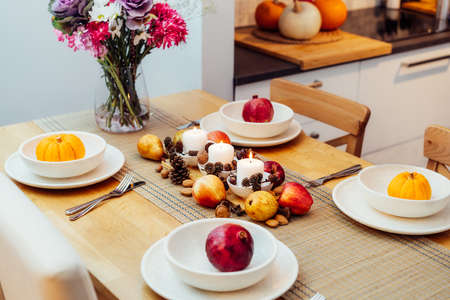 Fall table setting for celebration Thanksgiving day family party. Autumn composition with candles, fruits, nuts and cones. Plates with pumpkins and pomegranate. Natural autumn decor. Selective focusの写真素材
