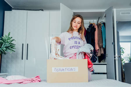 Woman selecting clothes from her wardrobe for donating to a Charity shop. Decluttering, Sorting clothes and Cleaning Up. Reuse, second-hand concept. Conscious consumer, sustainable lifestyleの写真素材