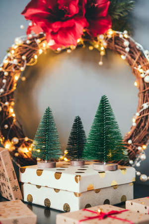 Decorative small Christmas trees on the gift box with elegant flower wreath on gray wall background. Festive home decor. Merry Christmas and New Year. Vertical card with copy space for writing text.の写真素材