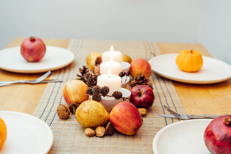 Fall table setting for celebration Thanksgiving day family party. Autumn composition with candles, fruits, nuts and cones. Plates with pumpkins and pomegranate. Natural autumn decor. Selective focusの写真素材