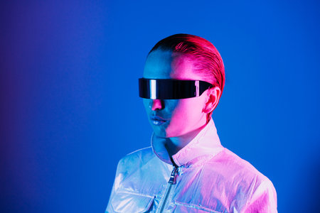 Neon portrait of woman, dressed in futuristic holographic clothes and glasses. Portrait of a cyberpunk girl. Neon blue and pink light. Virtual reality glasses. Fashion, futuristic generation concept.の写真素材