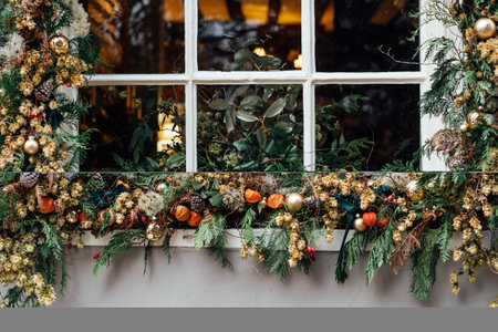 Winter holiday window decorated with fresh greens, red berries, cones and flowers. Outdoor exterior decoration made of natural materials. Christmas festive city. Selective focus.の写真素材