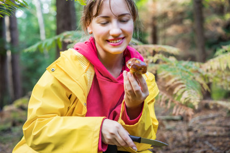 Portrait of young smiling woman holding just picked mushroom in the autumn forest. Picking season, leisure and people concept. Selective focus.の写真素材