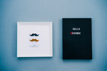 Different color male moustaches in the frame and letter board with Hello Movember message on the...