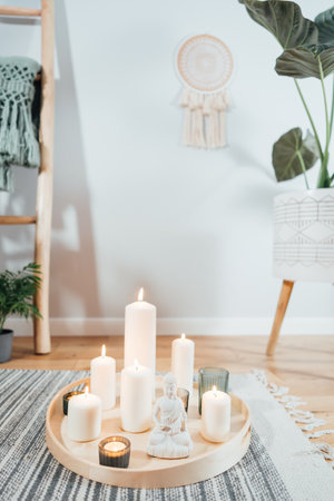 Wooden tray with burning candles and white Buddha statuette on the floor of modern Scandi interior. Zen Composition for meditation, yoga practice, relaxation. Balance and calm energy flow indoorの写真素材
