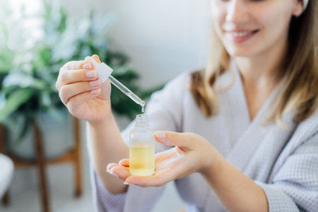 Close up young woman in bathrobe holding mockup bottle and dropper with hyaluronic acid serum in her hands. Skin hydrating. Cosmetic spa procedures. Beauty self-care at home. Selective focus.の写真素材