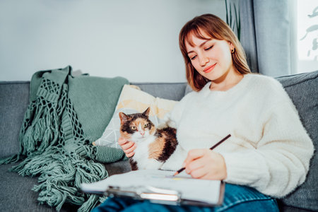 Relaxed young woman drawing work-life balance wheel sitting on the sofa with cat pet at home. Self-reflection and life planning. Coaching tools. Finding Balance in Your Life. Selective focusの写真素材