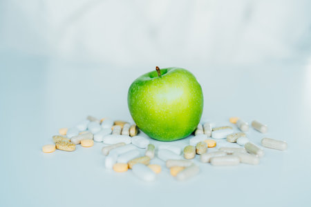 Green apple in the pile of different pills on the white. Choose between natural, folk and traditional synthetic way of vitamins, health care. Diet modification, diabetes management, drugs alternative.の写真素材