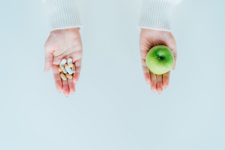 Female hands with green apple and different pills. Choose between natural, folk and traditional synthetic way of vitamins, health care. Diet modification, diabetes management, drugs alternativeの写真素材