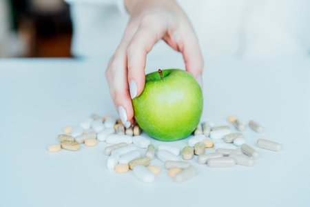 Female hand taking green apple from the pile of pills. Choose between natural, folk and traditional synthetic way of vitamins, health care. Diet modification, diabetes management, drugs alternative.の写真素材