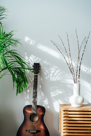 Modern minimalist Scandinavian style interior with branches of the pussy willow on a wooden console, green house plants and acoustic guitar near white wall with shadows on white wall. Vertical card.の写真素材