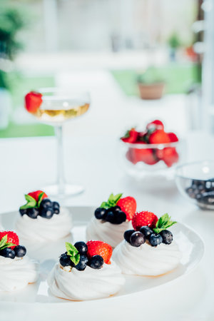 Meringue dessert Pavlova cake with fresh cream, strawberries and blueberries, decorated with mint on the white plate. Recipes for delicious light desserts. Confectionery cafe menu. Selective focusの写真素材