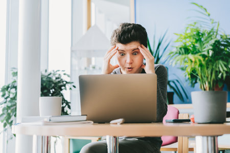 Middle aged shocked business woman sitting in front of laptop looking at screen at her workstation in office. Frustrated worried face expression emotion feelings problem perception reactionの写真素材