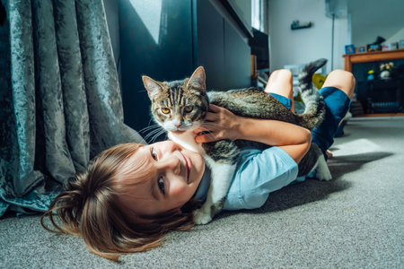 Portrait of a Happy smiling kid at home playing with a kitty cat. Caucasian boy lying on a carpeted...