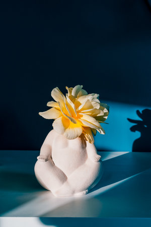 Ceramic plus size female body-shaped vase with flower in light and shadow on blue wall and table. Self-acceptance, body positivity. Serene, Balancing Body, Mind, Soul, Spirit. Mental Health Practiceの写真素材