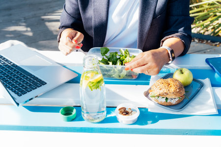 Healthy food concept: closeup woman eating from lunch box with healthy wholemeal burger bun, salad with fresh vegetables on the wooden picnic table outdoors. Balanced portion for weight loss diet.の写真素材