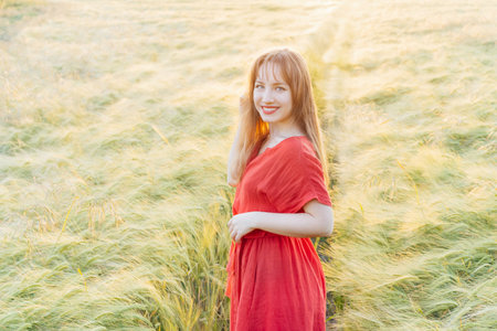 Young happy woman in red dress walking in wheat field on sunset. Breathe of freedom. Positive...