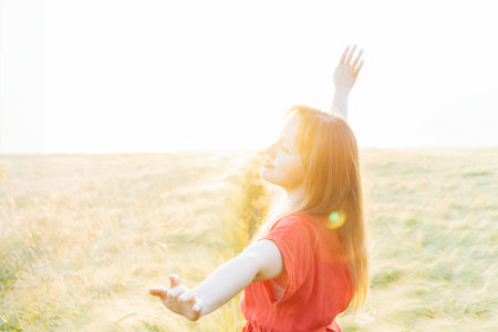 A happy young woman with raised arms relaxing in wheat field on sunset. Celebrating freedom....