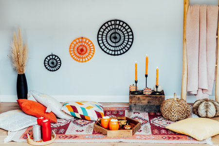 Decorated cozy autumn interior for relax during fall holidays. Comfy floor location with cushions, wicker pumpkins, burning candles. Thanksgiving, Halloween plans at home. Romantic date, movie nightの写真素材