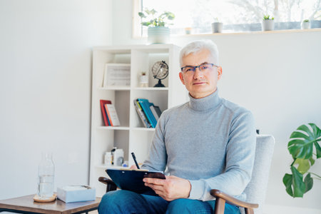 Professional Psychotherapy. Successful male Psychologist Smiling To Camera Sitting On armchair In Office. Mature 50s middle-aged professional portrait of teacher, coach, mentor, therapist, counselor