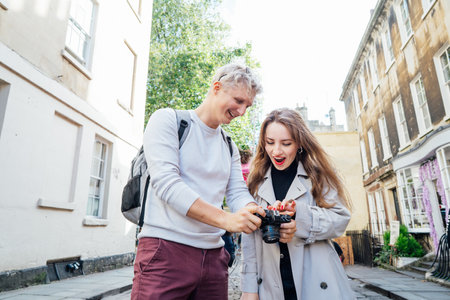 Young emotional friends watching pictures on a digital camera during travel walk in old European...