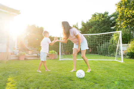 Young mother and son giving five during soccer game in the garden. Happy family playing football, having fun together. Fun Playing Games in Backyard Lawn on Sunny Summer Day. Motherhood, childhoodの写真素材