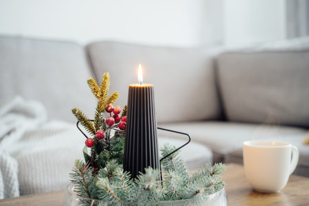 Composition of flaming black christmas candle and spruce branches and cup with hot drink on coffee...